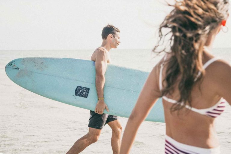 Man holding surfing board walking with his girlfriend. This is an usual type of lifestyle photography