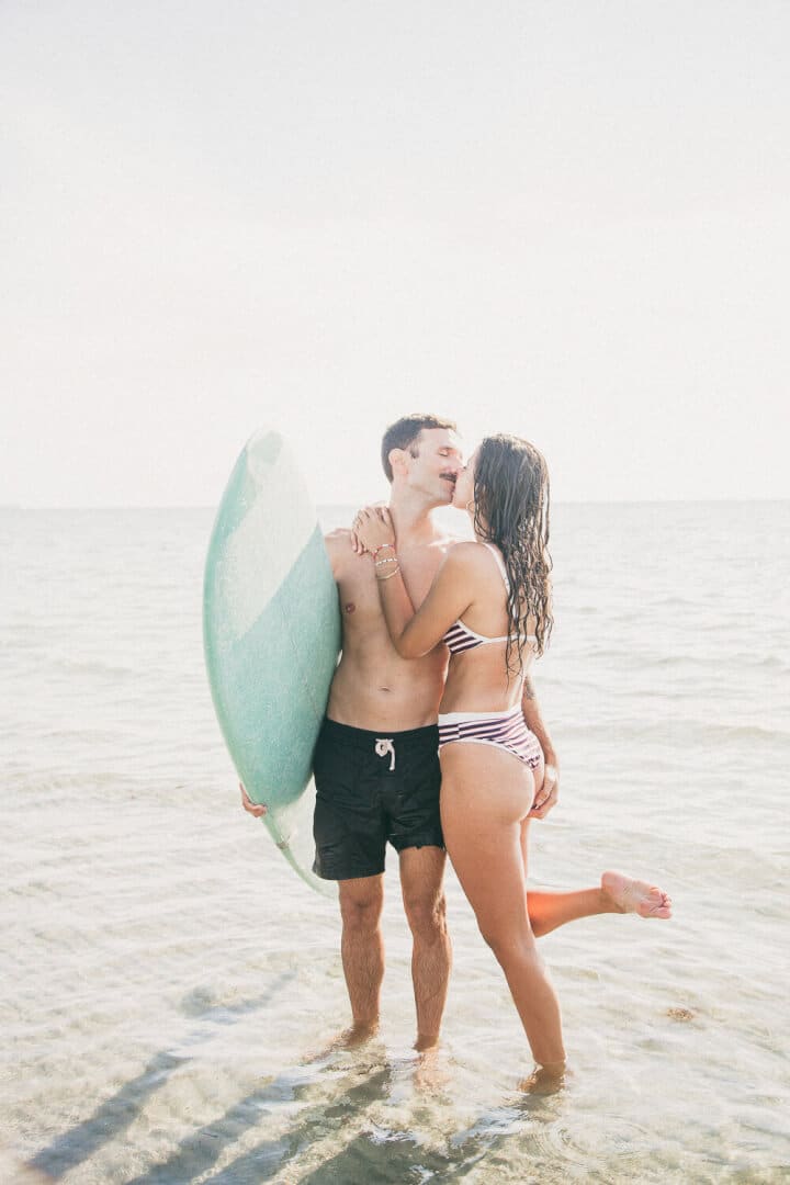 Couple on the beach holding a surf table and almost kissing