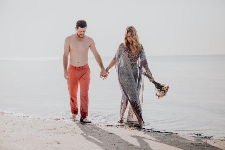 Couple walking towards the camera at the beach. One of them is holding flowers