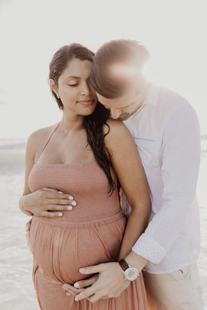 Loving parents-to-be enjoying their day out together on one of Miami's scenic beaches; expecting mother radiantly dressed for summer weather in a stylish sundress with her protective spouse at her side.