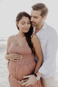 Pregnant woman wearing a chic sundress and holding hands with her delighted husband, taking pleasure in the marvelous views offered by Miami Beach's uninterrupted horizon line under sunny skies.