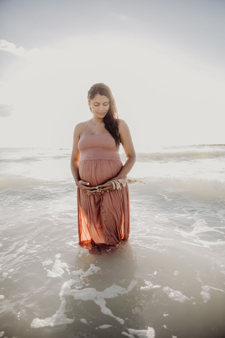 An expectant mom wearing a bright sundress on Miami Beach, enjoying the beautiful morning light and feeling her baby's movements within her womb.